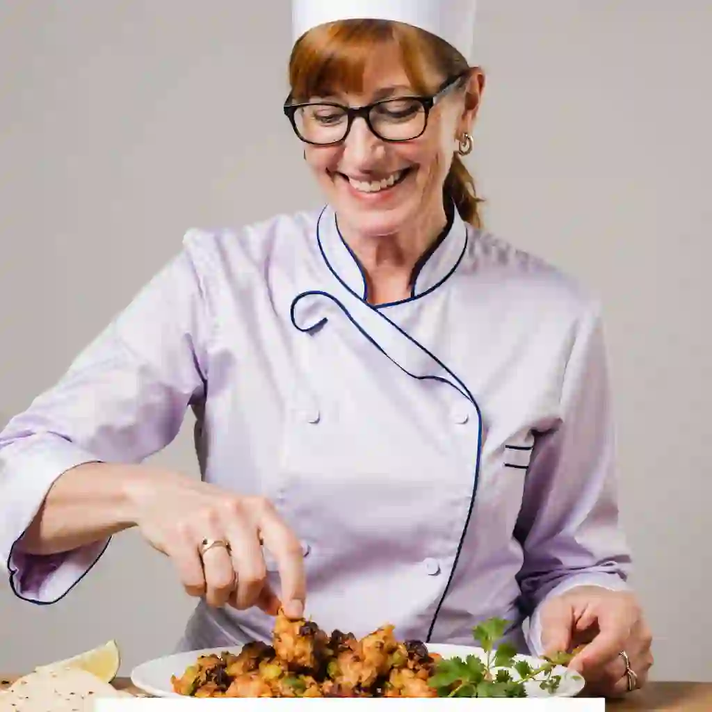 Woman serving a plate of fajitas de pollo in a cozy kitchen with tortillas and garnishes