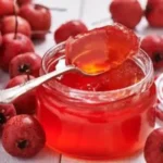 Mayhaw jelly in mason jar on rustic kitchen counter with biscuits