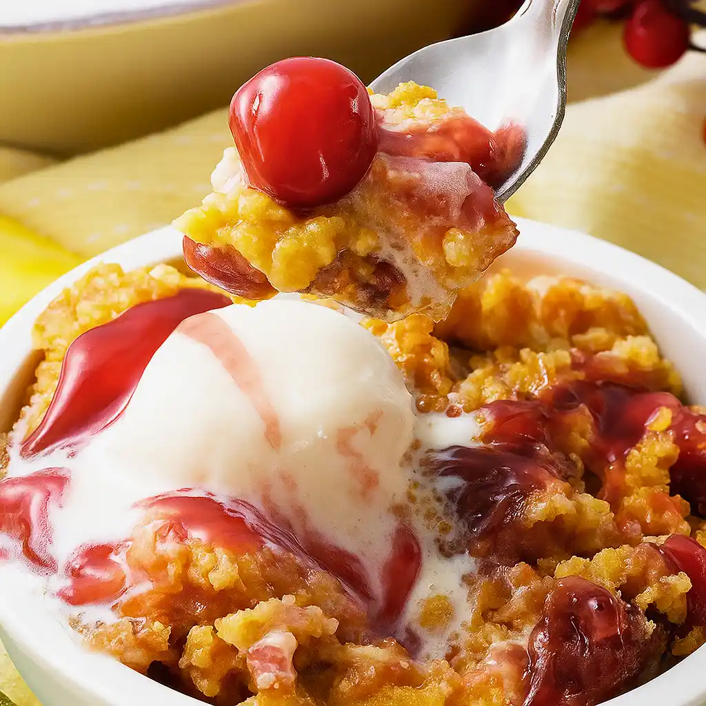 Spoonful of Cherry Pineapple Dump Cake with a cherry and vanilla ice cream, ready to be enjoyed.