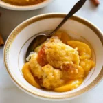A warm bowl of homemade peach cobbler topped with cinnamon, ready to be served with a spoon.