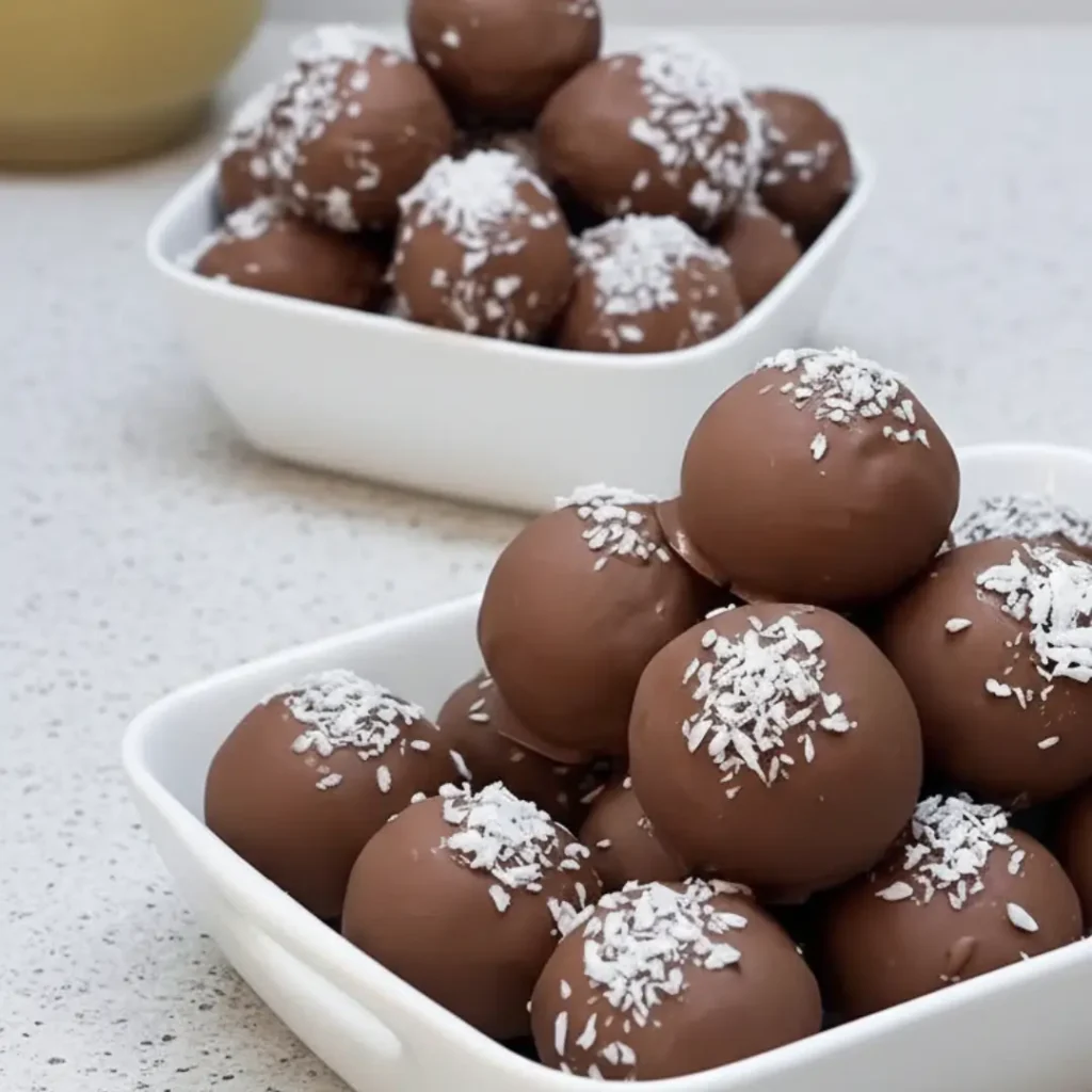 Two white bowls piled high with chocolate-covered Bounty balls sprinkled with shredded coconut, featuring a text overlay that reads "Bounty balls 3 ingredients