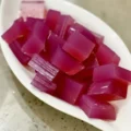 A white leaf-shaped bowl filled with vibrant, translucent cubed jelly made using a simple pink gelatin trick recipe.
