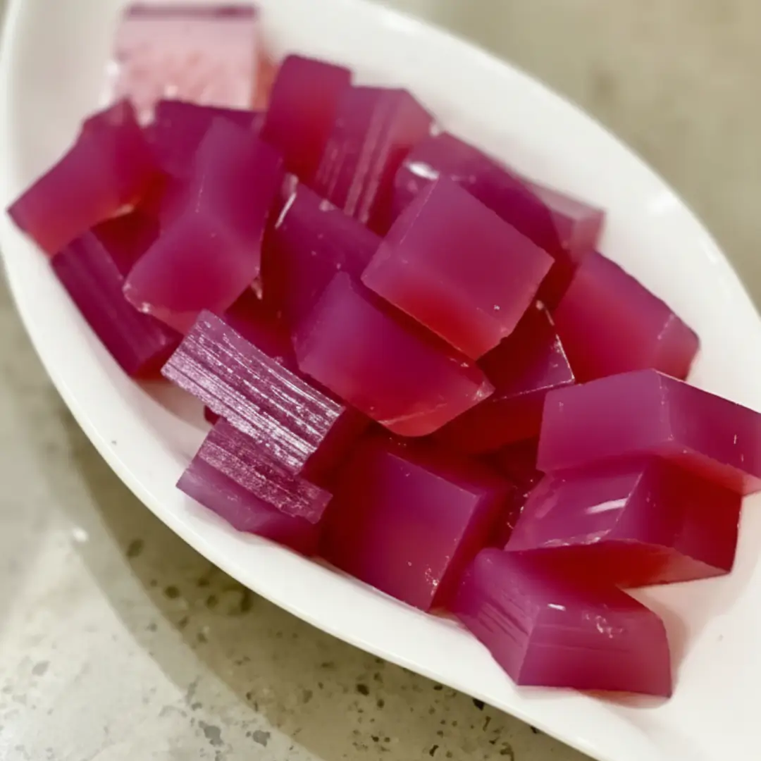 A white leaf-shaped bowl filled with vibrant, translucent cubed jelly made using a simple pink gelatin trick recipe.