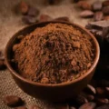 A rustic brown bowl overflowing with rich natural cocoa powder, surrounded by raw cacao beans on a textured burlap surface.