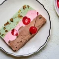 A slice of classic spumoni ice cream showing distinct layers of pistachio, cherry, and chocolate on a plate.