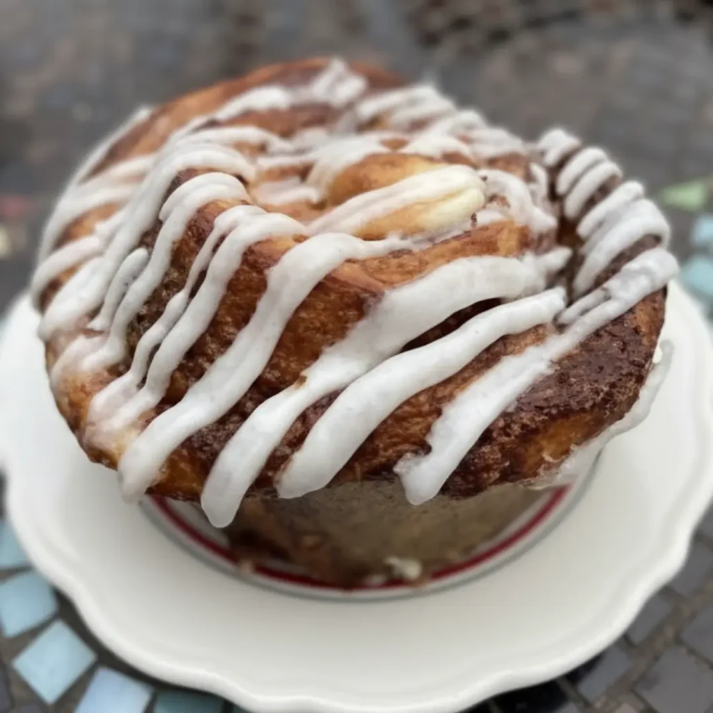 A close-up of a baked cinnamon bun dessert with white icing on a plate, representing the type of baked goods involved in the recent cinnamon bun dessert recall.