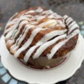 A close-up of a baked cinnamon bun dessert with white icing on a plate, representing the type of baked goods involved in the recent cinnamon bun dessert recall.