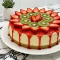 A freshly baked Mini Strawberry Kiwi Cheesecake with a vibrant red glaze dripping down the sides, topped with fresh fruit.