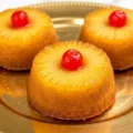 Close up of three perfectly baked mini pineapple upside down cakes served on a decorative gold platter.
