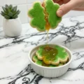 A hand breaking apart a green shamrock cookie to reveal a gooey golden filling, demonstrating a sweet St. Patrick's Day Sugar Cookie Recipe.