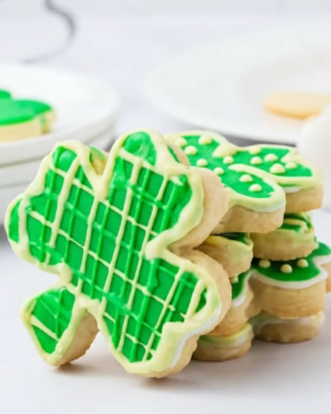 A close-up of a stack of homemade shamrock-shaped sugar cookies decorated with bright green icing in plaid and dotted patterns, a great alternative to st patrick's day cookies costco