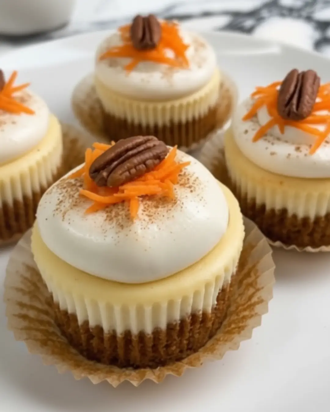 Close-up of four freshly baked Carrot Cake Cheesecake Cupcakes topped with creamy frosting, grated carrots, and a pecan.Close-up of four freshly baked Carrot Cake Cheesecake Cupcakes topped with creamy frosting, grated carrots, and a pecan.