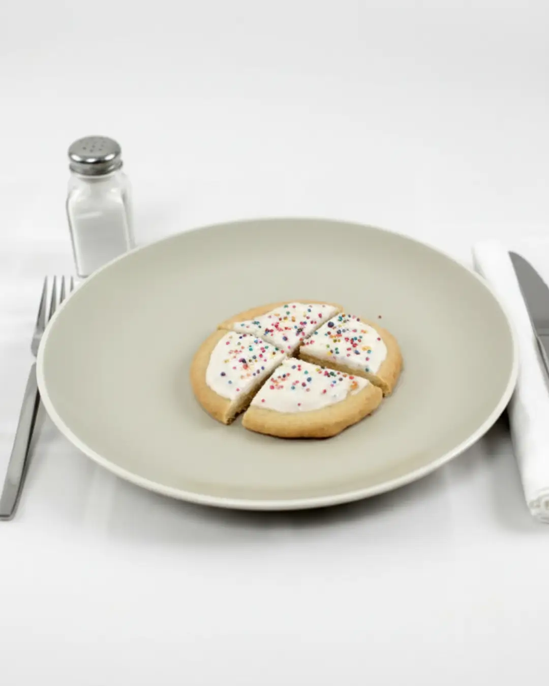 A frosted sugar cookie with colorful sprinkles cut into four pieces on a light plate, a helpful visual for understanding portion size and sugar cookie nutritional value.