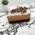 A close-up of a layered chocolate mousse cake slice with whipped cream and chocolate curls, representing good gluten free desserts, served on a marble countertop.