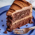 A delicious slice of layered chocolate cake with creamy chocolate frosting on a blue plate, showcasing the results of an easy chocolate cake recipe.
