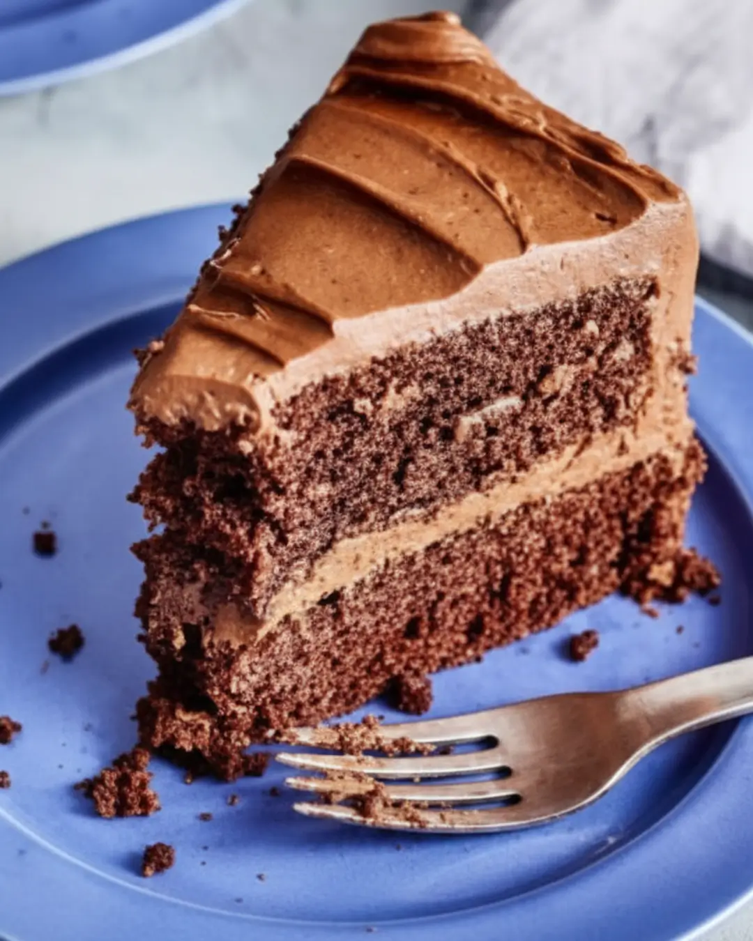 A delicious slice of layered chocolate cake with creamy chocolate frosting on a blue plate, showcasing the results of an easy chocolate cake recipe.