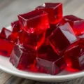 A close-up of vibrant red, translucent gelatin cubes piled high on a white plate over a wooden surface.
