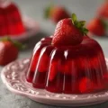 Close-up of a molded pink gelatin dessert filled with fresh strawberries, sitting on a decorative pink plate.
