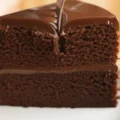 A close-up of a silver fork slicing through a rich, two-layer moist chocolate cake Recipe covered in thick, glossy fudge frosting.