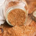A glass mason jar tipped over, spilling a freshly mixed homemade blend for a fajita seasoning recipe onto a wooden cutting board.