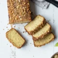 Overhead view of baking ingredients including a bowl of flour, eggs, butter, lime, and crushed nuts on a white wooden table, inspiring searches for a gluten free bakery near me.
