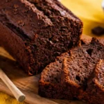 A partially sliced loaf of dark chocolate banana bread on a wooden cutting board.