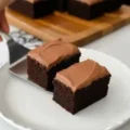 A serving spatula placing a frosted slice of the best chocolate cake recipe onto a white plate next to another slice.