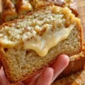 A close-up of a hand holding a thick slice of the Best Ever Banana Bread, revealing a warm, gooey, melted center dripping down the crumb.