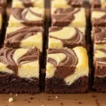 Close-up of freshly baked Easy Mini Cheesecake Brownies with a swirled cream cheese and chocolate top, resting on a wooden board.