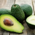 Close-up of fresh whole avocados and one halved avocado with a pit on a wooden table, useful for visualizing portion sizes when counting calories in an avocado.