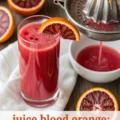 A hand using a manual juicer to squeeze fresh juice from a blood orange, next to a tall glass of the bright red juice.