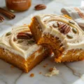 Two frosted Gluten Free Pumpkin Bars topped with pecans and pumpkin seeds resting on a marble countertop.
