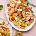 A finished Summer Peach Salad served on a white oval platter, featuring sliced peaches, tomatoes, mozzarella, red onions, and basil.