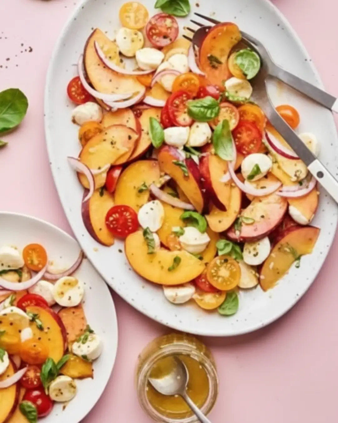 A finished Summer Peach Salad served on a white oval platter, featuring sliced peaches, tomatoes, mozzarella, red onions, and basil.