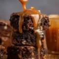 Close up of thick caramel brownies cut in half, revealing chocolate layers and gooey liquid caramel oozing from the center.