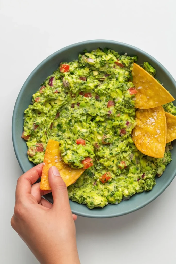 Mashing avocados with a fork in a glass bowl to achieve the perfect chunky texture.