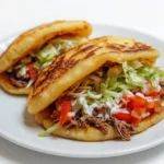 A vibrant stack of authentic Mexican gorditas sliced open and stuffed with shredded beef, lettuce, and crema on a rustic wooden table.
