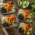 Four glass containers filled with rice, black beans, and colorful roasted vegetables on a wooden table, showcasing an easy vegetarian meal prep.