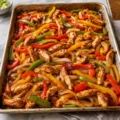 Freshly baked oven chicken fajita recipe on a large metal sheet pan with colorful bell peppers